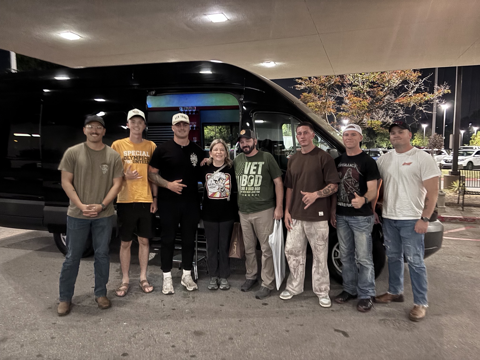 A group of guests standing beside a black TPL Sprinter at night
